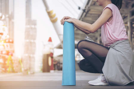 Woman hands rolled up yoga mat outdoor workout. Close up hands rolling foam yoga gym mat outside morning exercise. Woman stretching workout sportive healthy lifestyle on street city town park conceptの写真素材