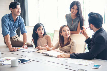 Happiness diversity business team meeting corporate office desk in company meeting room. Asian team group partner brainstorming discussion multiethnic people sitting share ideas teamwork in boardroomの写真素材