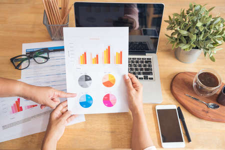 Woman working at home office desk using laptop business financial document chart and graph on wooden table with coffee cup. Woman freelance reading business graphs sale report on business office deskの写真素材