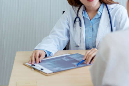 Two asian women doctors discuss meeting doctor's office medical clinic looking x-ray film consulting patient disease. Asian medical lab young women talking together discussing healthcare teamworkの写真素材
