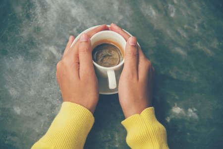 Close up hands of woman sitting office desk holding sweet coffee cup relax and enjoy with happy time. Hot coffee mug in hand. Woman holding coffee cup relaxing after work at office warm taste in cafeの写真素材