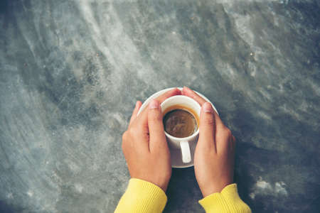 Close up hands of woman sitting office desk holding sweet coffee cup relax and enjoy with happy time. Hot coffee mug in hand. Woman holding coffee cup relaxing after work at office warm taste in cafeの写真素材