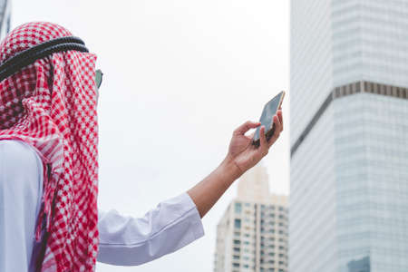 Islamic man using smartphones app organize schedule agenda  focus on hands holding smartphone muslim modern uae city. Arab men wear hijab and muslim formal dress sending text sms online lifestyleの写真素材