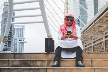 Islamic man using smartphones app organize schedule agenda  focus on hands holding smartphone muslim modern uae city. Arab men wear hijab and muslim formal dress sending text sms online lifestyleの写真素材