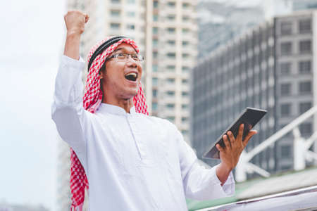 Islamic man using smartphones app organize schedule agenda  focus on hands holding smartphone muslim modern uae city. Arab men wear hijab and muslim formal dress sending text sms online lifestyleの写真素材