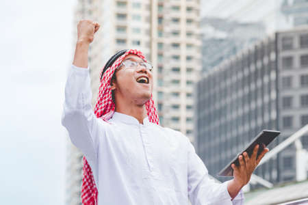 Islamic man using smartphones app organize schedule agenda  focus on hands holding smartphone muslim modern uae city. Arab men wear hijab and muslim formal dress sending text sms online lifestyleの写真素材