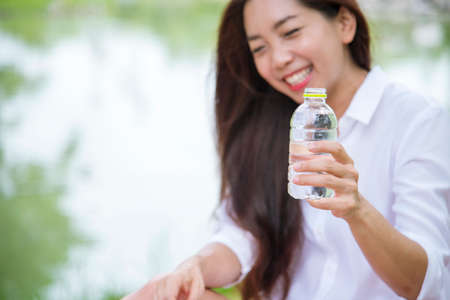 Happiness Beautiful asian chinese women holding mineral water bottle. Young Woman Drinking Water from bottle in green garden Park. Asian female drinking water bottle healthy person happy and smilingの写真素材
