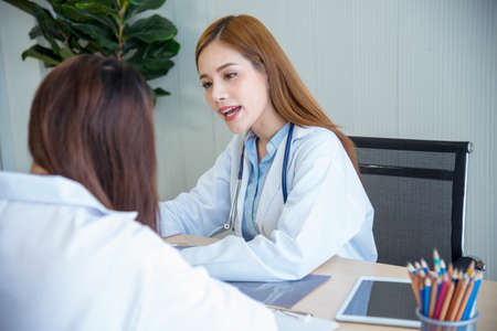 Two asian women doctors discuss meeting doctor's office medical clinic looking x-ray film consulting patient disease. Asian medical lab young women talking together discussing healthcare teamworkの写真素材
