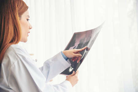 Two asian women doctors discuss meeting doctor's office medical clinic looking x-ray film consulting patient disease. Asian medical lab young women talking together discussing healthcare teamworkの写真素材