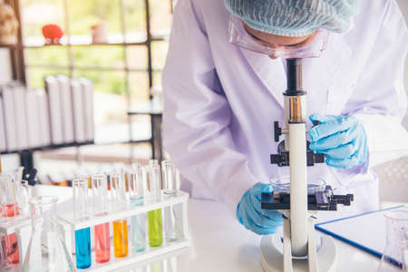 Closeup Woman scientist hand use dropper in lab look at science microscope medical test, research biology chemistry. Females technician laboratory analyzing blood scientific pharmaceutical research.の写真素材