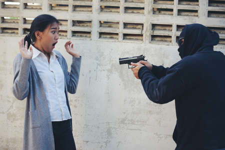Thief armed man rob woman by gun on street so scared shocked face. Frightened asian woman was rob aggressive by danger bandit man. Robbery thief using gun burglar. Criminal aggression crime concept.の写真素材