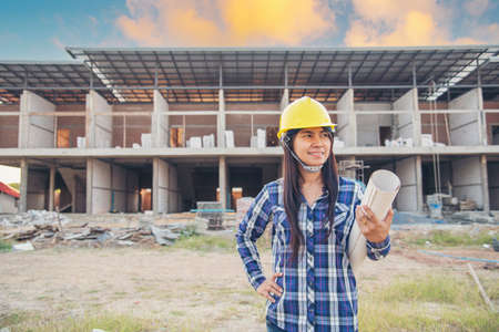 Woman construction engineer hold blueprint wear plaid shirt safety white hard hat at construction site industry labor worker. Architecture Female engineer civil worker look at blueprint real estateの写真素材