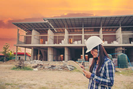 Woman construction engineer hold blueprint wear plaid shirt safety white hard hat at construction site industry labor worker. Architecture Female engineer civil worker look at blueprint real estateの写真素材
