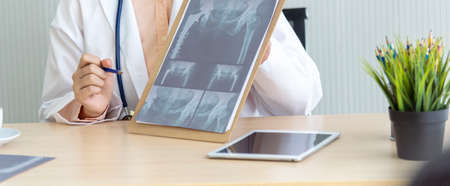 Two asian women doctors discuss meeting doctor's office medical clinic looking x-ray film consulting patient disease. Asian medical lab young women talking together discussing healthcare teamworkの写真素材