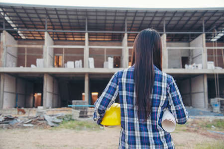 Woman construction engineer hold blueprint wear plaid shirt safety white hard hat at construction site industry labor worker. Architecture Female engineer civil worker look at blueprint real estateの写真素材