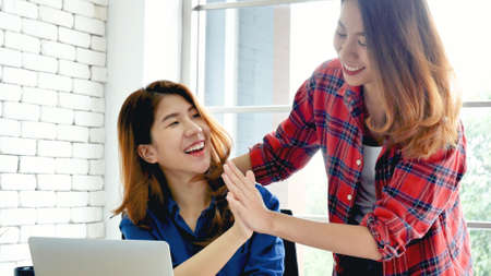 Two businesswomen talking together at office desk got happiness good news. Woman meeting make high five for good news. High five success two working woman partner meeting team solidarity power conceptの写真素材