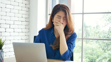Woman streching arm raised sitting incorrect position home office desk. Back side of young asian woman tired from work body stress back pain office syndrome. Female work from home new normal conceptの写真素材