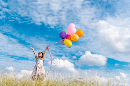 Cheerful cute girl holding balloons running on green meadow white cloud and blue sky with happiness....