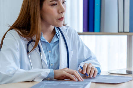 Two asian women doctors discuss meeting doctor's office medical clinic looking x-ray film consulting patient disease. Asian medical lab young women talking together discussing healthcare teamworkの写真素材