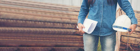 Banner Civil Engineer woman hands holding white hardhat worker helmet on Construction site. Panorama industry engineer woman hands holding worker helmet hard hat. Wire mesh background with copy spaceの写真素材