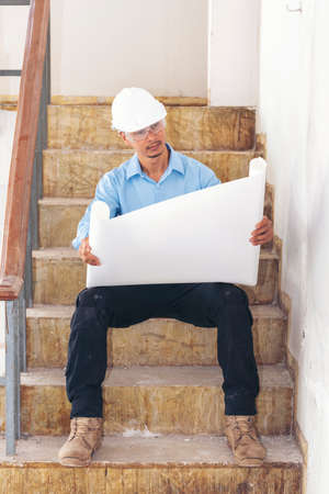 Construction engineer man hold blueprint wear blue shirt safety white hard hat at construction site...