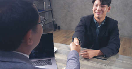 Asian man colleague friendship meeting at work. Happiness two men colleague working together team meeting in office desk. Team business partners working with computer laptop startup small company.の写真素材