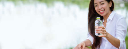 Banner Young Woman Drinking bottle water in green garden park. Panorama Asian female drink water bottle healthy person smiling. Happy Beauty Asian chinese women hold mineral water bottle copy spaceの写真素材