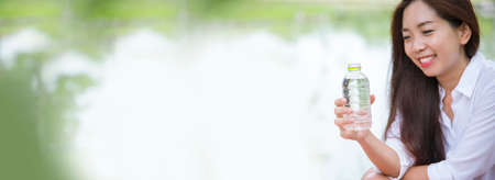Banner Young Woman Drinking bottle water in green garden park. Panorama Asian female drink water bottle healthy person smiling. Happy Beauty Asian chinese women hold mineral water bottle copy spaceの写真素材