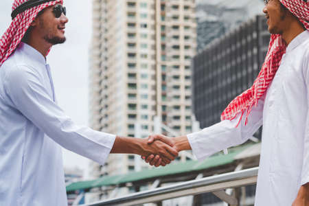 Arab Businessman Muslim dress shaking hands together. Muslim Men Teamwork business partner handshake with business Partnership. Close up hand UAE diversity multiracial people trust honesty commitmentの写真素材
