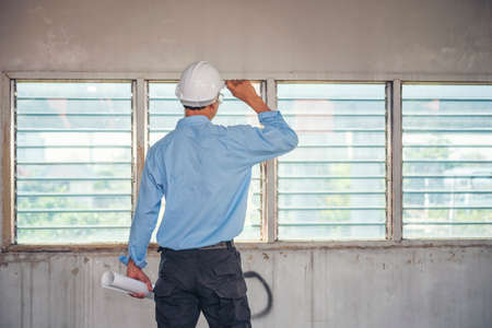 Construction engineer man hold blueprint wear blue shirt safety white hard hat at construction site industry labor worker. Architecture man engineer civil worker look at blueprint real estate conceptの写真素材