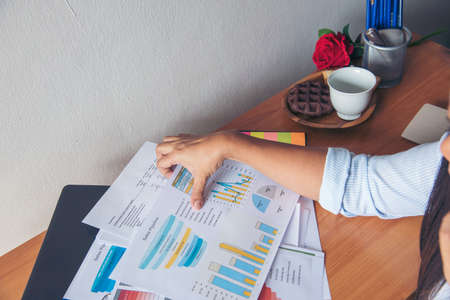 Business woman using smartphone, laptop on office desk. Female freelance reading financial graph charts Planning analyzing marketing data. Hands of young woman working in office firm business info.の写真素材