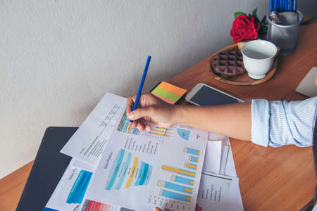 Business woman using smartphone, laptop on office desk. Female freelance reading financial graph charts Planning analyzing marketing data. Hands of young woman working in office firm business info.の写真素材