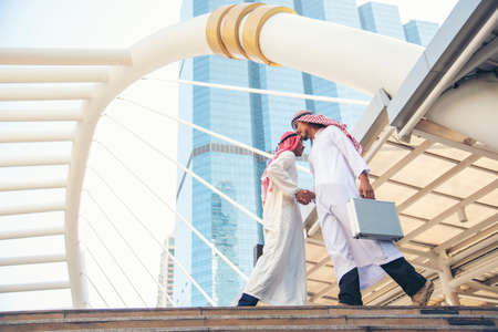 Arab Businessman Muslim dress shaking hands together in modern city UAE background. Muslim Men Teamwork business partner handshake with Partnership. diversity multiracial arab people trust commitmentの写真素材