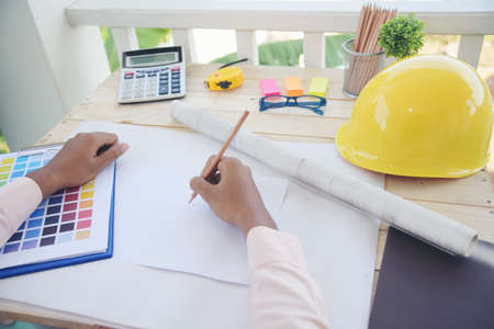 Civil construction engineer working with laptop at desk office with white yellow safety hard hat at office on construction site. Asian young man architecture project manager sitting at office on siteの写真素材