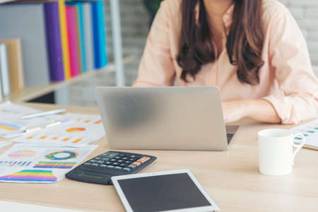 Asian Female freelance using laptop at home office desk. Woman reading financial graph chart Planning analyzing marketing data. Asian female people working office firm with business stuff, coffee cupの写真素材