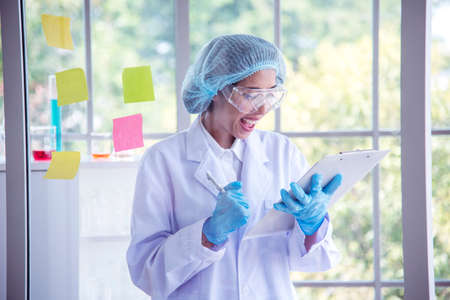 Woman scientist hand write note information in medical lab look at science microscope medical test, research biology chemistry. Asian Females technician laboratory analyzing blood test pharmaceuticalの写真素材