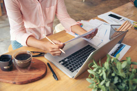 Business woman using smartphone, laptop on office desk. Female freelance reading financial graph...