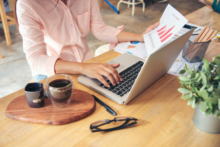 Businesswoman reading financial graph charts Planning analyzing marketing data. Women hands using smartphone, laptop on office desk. Hands of young asian woman working in office firm business info.の写真素材
