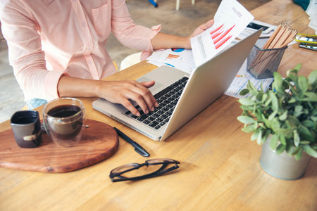 Businesswoman reading financial graph charts Planning analyzing marketing data. Women hands using smartphone, laptop on office desk. Hands of young asian woman working in office firm business info.の写真素材