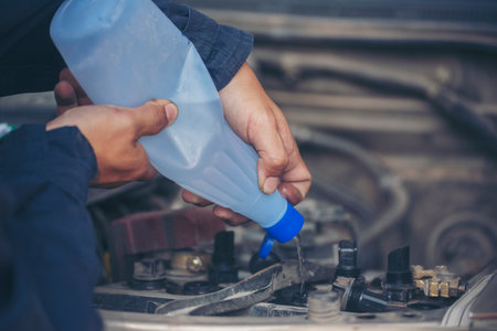 Car Mechanic man hands pouring Deionized purified Distilled water for car battery mechanical service. Close up hands man hold Deionized Distilled liquid water bottle at garage auto mobile car serviceの写真素材