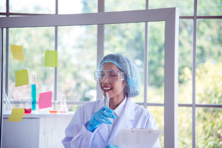 Woman scientist hand write note information in medical lab look at science microscope medical test, research biology chemistry. Asian Females technician laboratory analyzing blood test pharmaceuticalの写真素材
