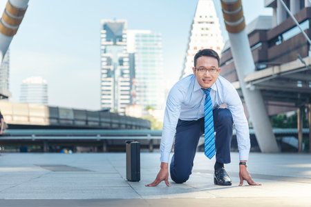 Businessman start kneeling city street race business goal winner challenge. Asian man look at camera smile face wear glasses. Man happiness time start up a business goal. Businessman race conceptの写真素材