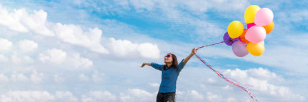Banner Cheerful cute girl holding balloons running green meadow white cloud and blue sky with...