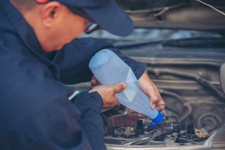 Car Mechanic man hands pouring Deionized purified Distilled water for car battery mechanical service. Close up hands man hold Deionized Distilled liquid water bottle at garage auto mobile car serviceの写真素材