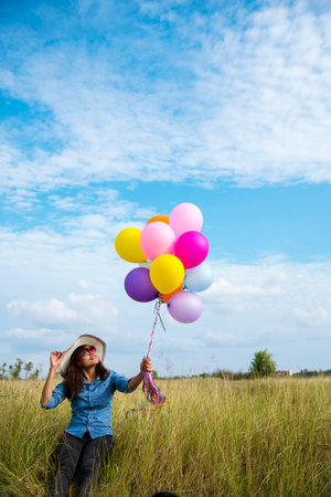 Woman holding balloons running on green meadow white cloud and blue sky with happiness Cheerful and relax. Hands holding vibrant air balloons play on birthday party happy times summer sunlight outdoorの写真素材