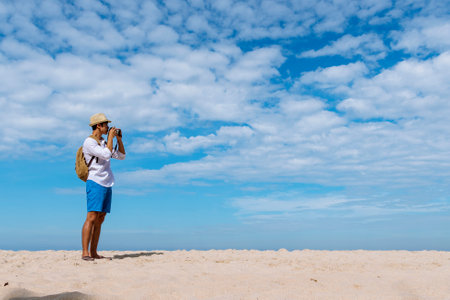 Man traveler using digital camera on summer beach blue sky take a photo. Asian Photographer man journey relax on the beach in summertime. Man backpack shooting photo asia destination holiday tripの写真素材