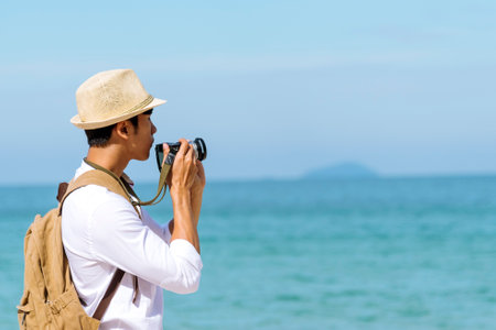 Man traveler using digital camera on summer beach blue sky take a photo. Asian Photographer man journey relax on the beach in summertime. Man backpack shooting photo asia destination holiday tripの写真素材