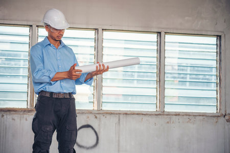 Construction engineer man hold blueprint wear blue shirt safety white hard hat at construction site industry labor worker. Architecture man engineer civil worker look at blueprint real estate conceptの写真素材