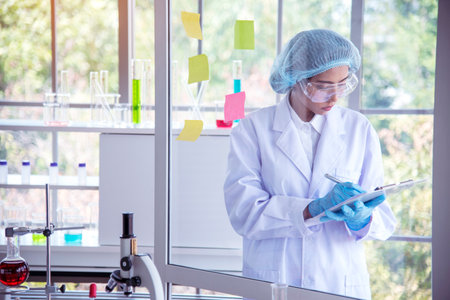 Asian Woman scientist hand write note research in medical lab look at science microscope medical test. Researcher biology chemistry. Asian Female technician laboratory using microscope blood testの写真素材