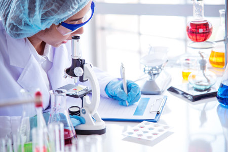 Asian Woman scientist hand write note research in medical lab look at science microscope medical test. Researcher biology chemistry. Asian Female technician laboratory using microscope blood testの写真素材